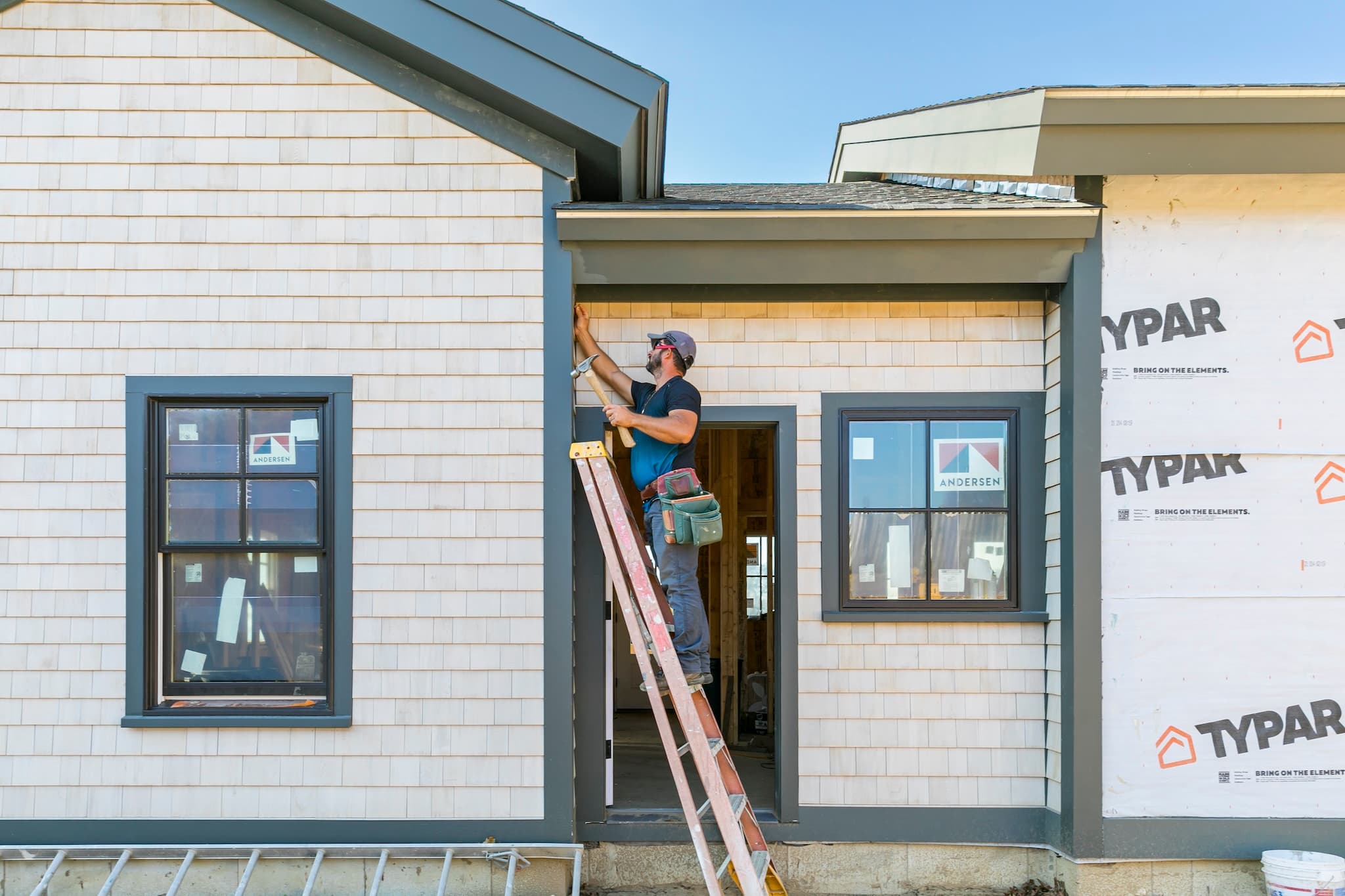 Tekton employee on a ladder installing shingles