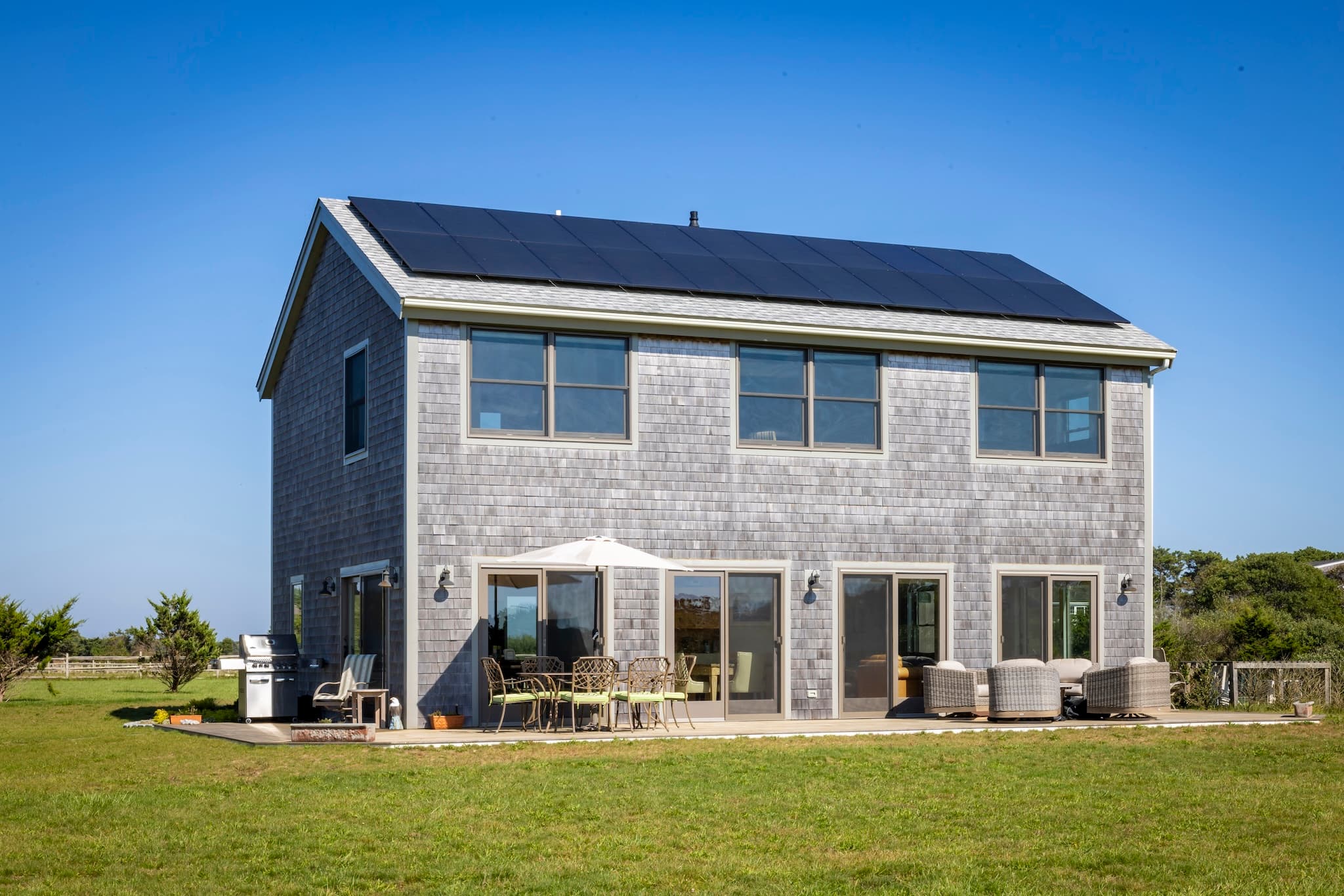 Katama home featuring solar panels, large windows, sliding doors, and a patio