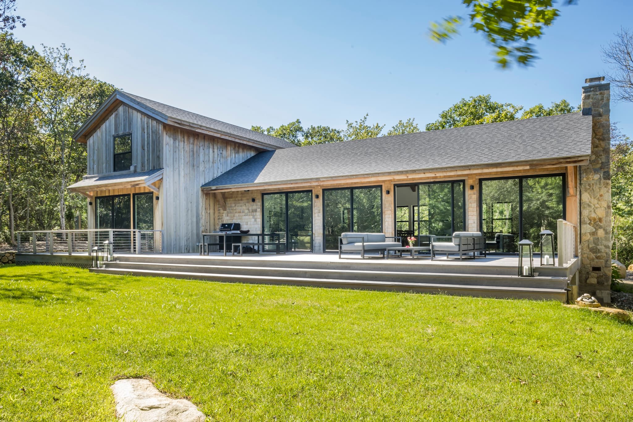 Rear exterior of a modern up-island home with large deck, patio furniture, and green grass